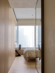 Modern minimalist bedroom with light wood floors, glass window overlooking cityscape, and metal furniture.