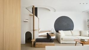 A minimalist living room with wood elements, featuring a white sofa, a black circular wall element, and a cat sitting on a wo