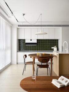 A modern minimalist residential kitchen with wood cabinets and a green tile backsplash.