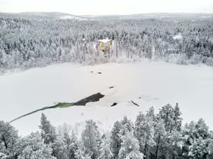 Aerial view of a snow-covered residential house nestled in a frozen forest.