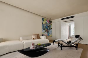 A modern living room with a neutral-toned color palette featuring a white sofa, abstract painting, and black coffee table wit