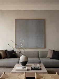 A modern monochromatic living room featuring a textured fabric sofa and a minimalist vase with white blossoms on a coffee tab