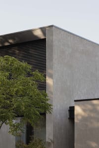Modern residential building exterior with concrete facade and dark window blinds.