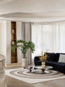 A modern living room with a wooden floor, a black sofa, and a circular coffee table with a plant and a vase.