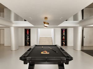 A minimalist playroom featuring a black pool table with billiard balls and cues, surrounded by concrete pillars and shelves d