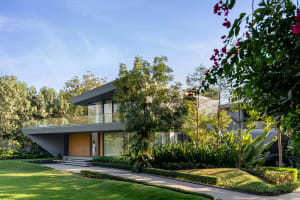 A modern house with concrete and glass features, surrounded by a lush green garden.