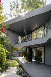 A modern residential exterior featuring concrete architecture, a balcony, and lush greenery.