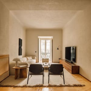 Modern minimalist living room with marble and wood furniture, featuring a white sofa, two black chairs, and a television in a
