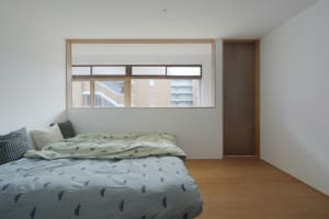 Minimalist bedroom with white walls, wooden floor, and a bed with green and blue bedding.