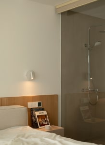 A modern minimalist bedroom with a wooden headboard and a glass-enclosed shower.