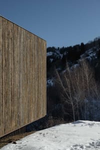 Modern minimalist building made of wood, with a clear blue sky in the background.