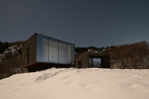 Modern residential architecture with glass and wood exterior at night in a snowy landscape.