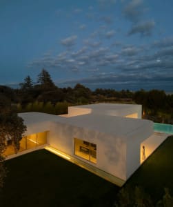 A modern residential house with concrete exterior walls and a pool at night with lights on.