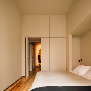 A minimalist bedroom with a bed, pillows, and a large cabinet on a wooden floor.