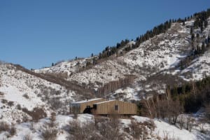 Modern house with wooden exterior and glass windows, nestled on a snowy hillside.