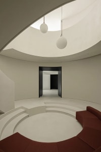 A minimalist living room with a circular seating area, white concrete steps, a red fabric seating area, and two hanging round
