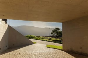 A view through a modern architecture structure showing concrete pavement and distant mountains.