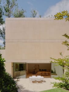 Modern house with concrete exterior, featuring a minimalist design with a large glass window and surrounding greenery.