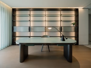 A modern office setting featuring a sleek, glass-desk workstation with a minimalist design, illuminated by warm lighting and 