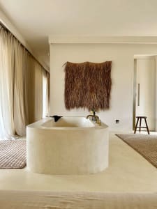 Minimalist bathroom interior with a large concrete bathtub placed on a concrete floor, accompanied by a large woven rug and a