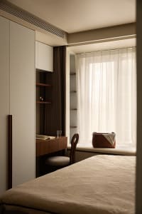 A minimalist bedroom with a bed, a chair, a desk, and a window with sheer curtains.