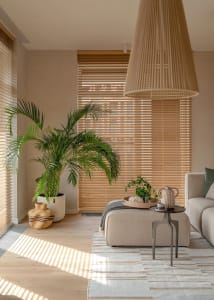 A modern, minimalist living room with neutral-toned furniture and decor, featuring a large potted palm plant and wooden floor