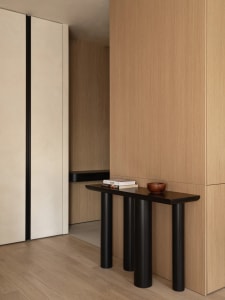 Modern indoor console table with wood surface and black cylindrical legs, positioned in a minimalist room with wooden walls a