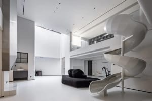 A minimalist, all-white residential interior featuring a spiral slide and black bean bag chairs.