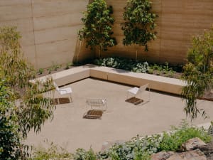 A minimalist outdoor patio with a concrete floor, white chairs, and greenery.