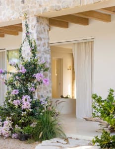 A residential entrance featuring a stone wall adorned with purple flowers, wooden beams, and a white curtain.