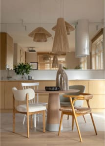 Modern dining room featuring a round wooden table with woven-straw pendant lights, fabric chairs, and concrete countertops.