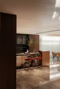 Modern living room featuring a sleek bar counter with marble top and two red stools, set against a warm, minimalist interior 