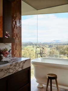 A luxurious bathroom featuring marble and concrete finishes, with a view overlooking trees and hills.