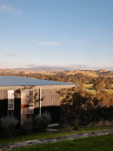 A modern house with a wooden exterior and metal roof in a rural landscape.
