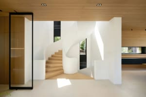 A modern minimalist interior featuring white concrete walls, timber floors, and a spiral staircase.