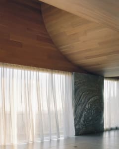Minimalist interior space featuring wood-paneled walls and ceiling, with transparent fabric curtains.