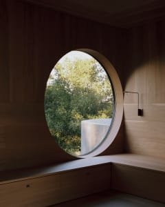 Circular window with wooden frame overlooking green trees.