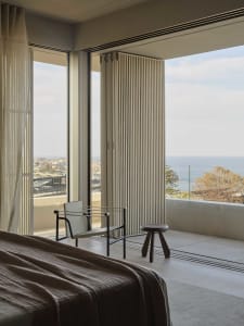 A modern bedroom featuring wooden flooring, minimalist furniture, and a view of the ocean.