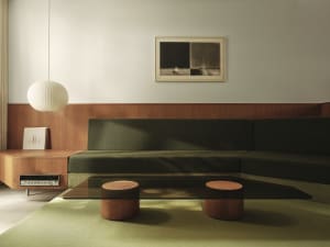 Modern green sofa with a glass coffee table and a wooden side table with a round lamp shade and a piece of art on the wall.