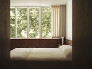 A minimalist bedroom featuring modern minimalistic elements, wooden headboard, fabric bedding, and glass elements.
