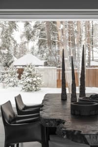 A cozy winter cabin scene with snow-covered trees, a black leather chair, and black candles on a wooden table.
