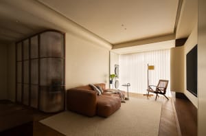 A minimalist living room with a brown leather sectional sofa, a wooden floor, and a wooden floor lamp.