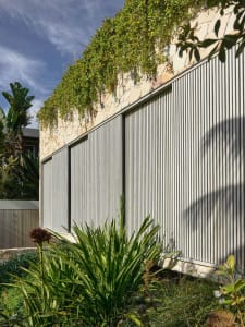 A modern exterior featuring a metal fence, stone wall, and greenery on top.