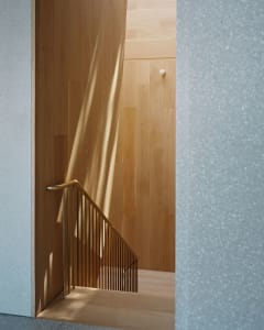 A modern wooden staircase with a metal railing against a wall with textured concrete and wooden flooring.
