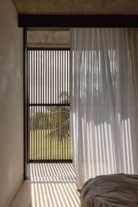 A bedroom interior featuring a transparent curtain, concrete walls, and modern lighting.