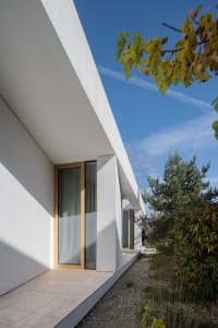 Modern house with white walls, glass windows, and concrete roof in a garden setting.