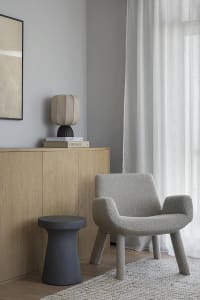 A modern living room featuring a taupe textured armchair and stool, wooden sideboard, and neutral color palette.