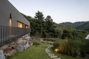 A modern residential exterior showcases a serene backyard garden pathway adorned with stones and surrounded by lush grass.