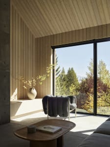 A modern living room with wooden walls and floor, featuring a grey armchair and a coffee table with a book.