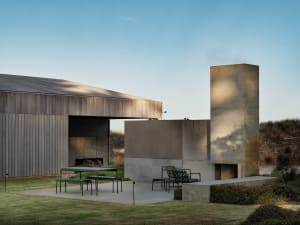 A modern residential exterior with a concrete fireplace and green seating area.